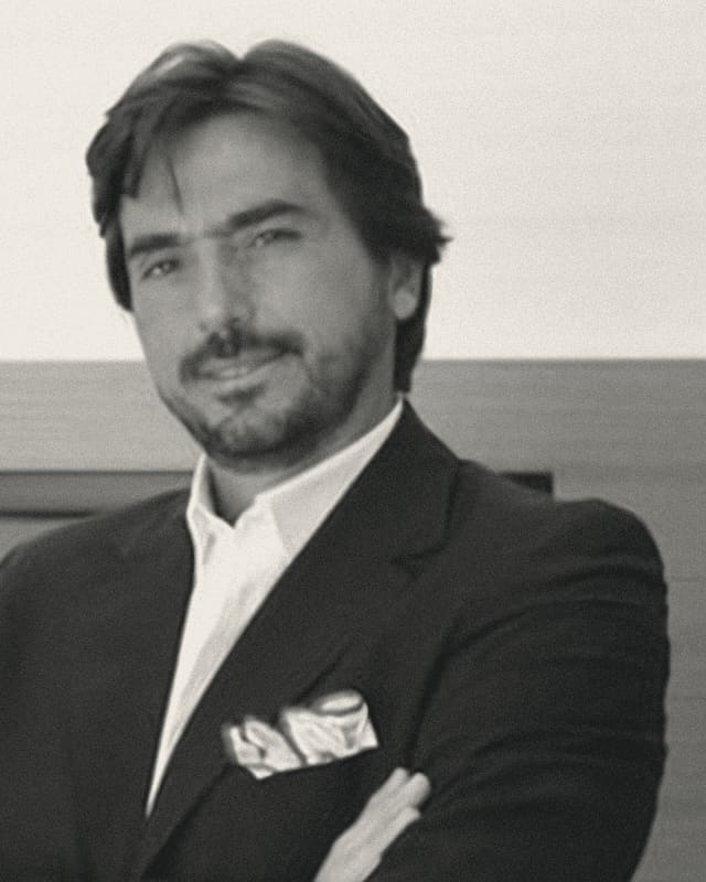 Portrait of Luigi Adamo in a dark jacket and white shirt, arms folded.